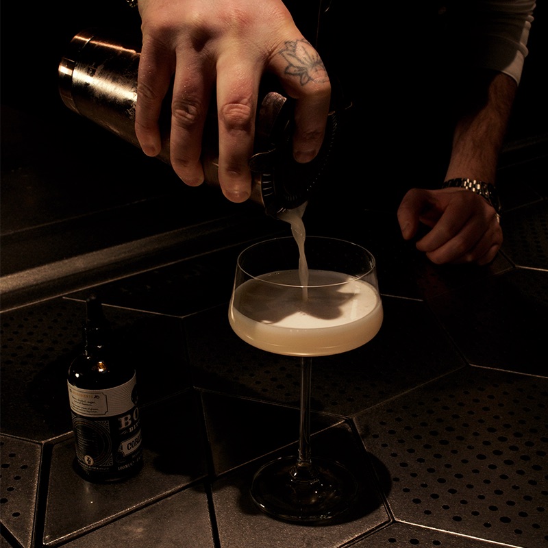 Clarified Mango, Passion Fruit Sours Cocktail Pour The Clarified Mango, Passion Fruit Sours Cocktail being poured from a bar shaker into a glass