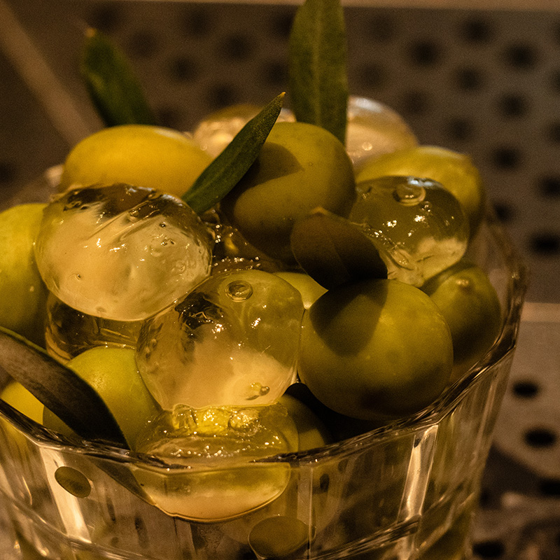 A glass bowl containing a mix of fresh and reverse-spherified Nocellara Del Belice olives