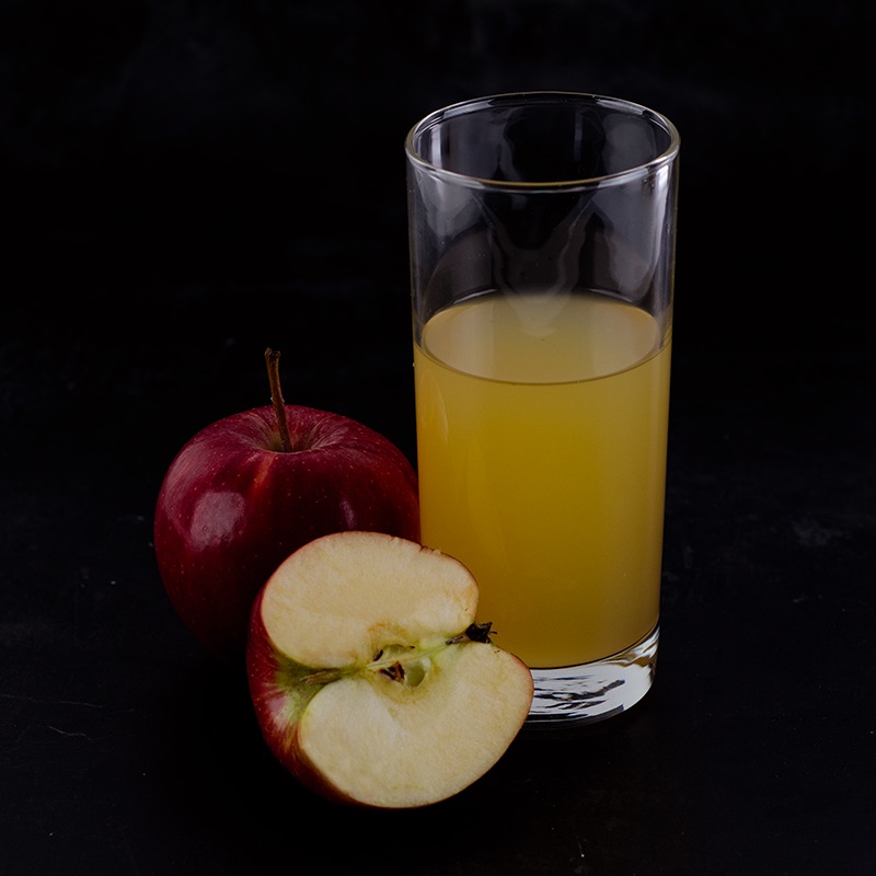 Apple alongside and apple sliced in half showing the inside and a glass of enzyme yielded and clarified apple juice