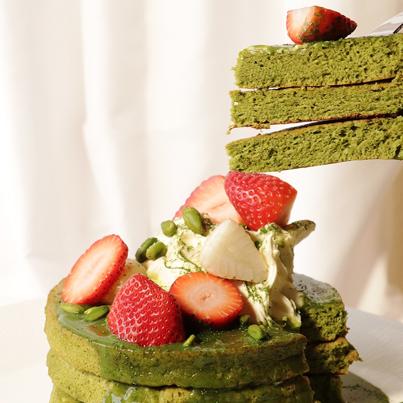 Pistachio and Matcha Pancakes with toppings, sliced into with a section lifted out by a fork to show inside.