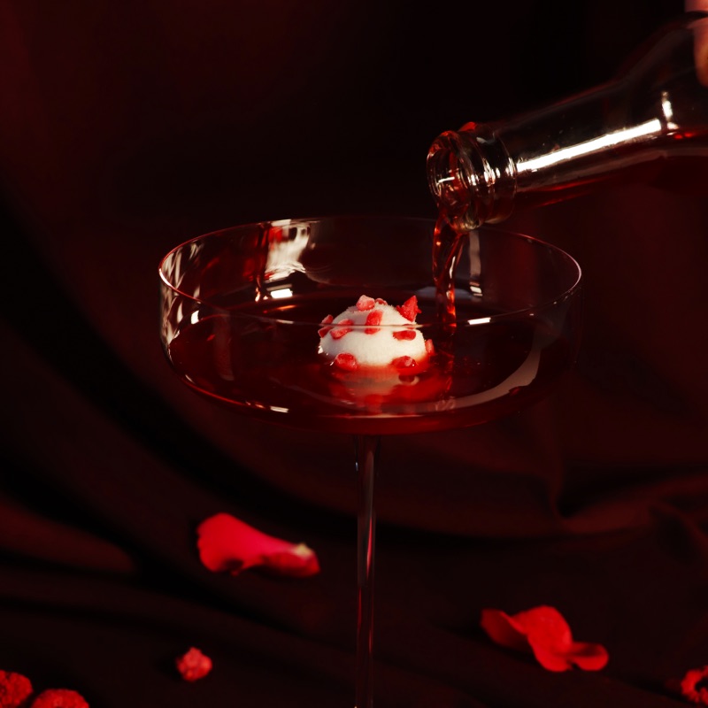 The Hibiscus Kombucha being pour from a bottle into a cocktail glass