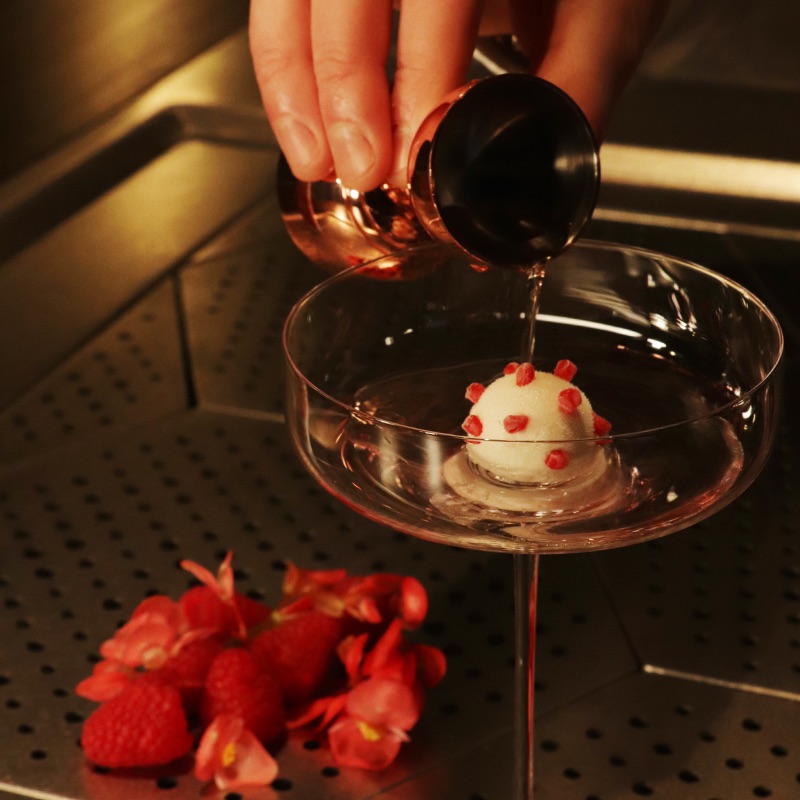 An image of Lychee and Raspberry Vodka being poured from a bar jigger into the cocktail glass