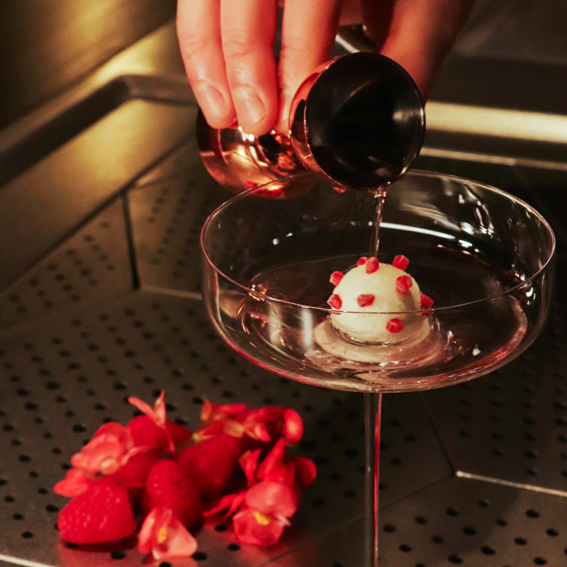 An image of Lychee and Raspberry Vodka being poured from a bar jigger into the cocktail glass