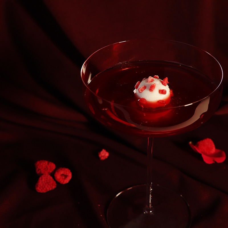 Raspberry, lychee and hibiscus "Sgroppino" Cocktail on a red fabric background surrounded by rose petals and raspberries