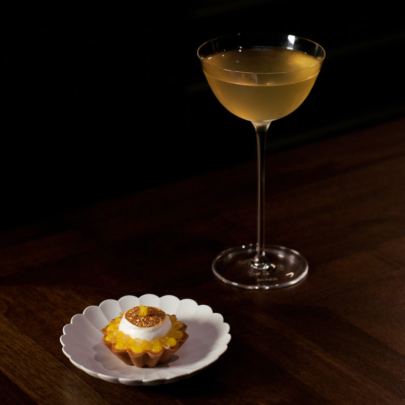 The Yuzu Meringue Pie Milk Punch Cocktail serves in a tall glass alongside a Yuzu Meringue Pie Tartlet